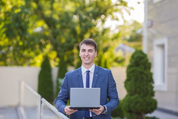 Successful businessman standing in the street holding a laptop