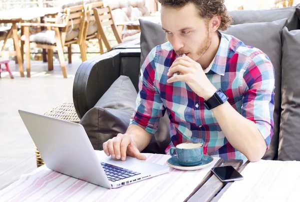 Style man with laptop sitting in a cafe  outdoor and smoking electronic cigarette. Handsome man working in cafe.