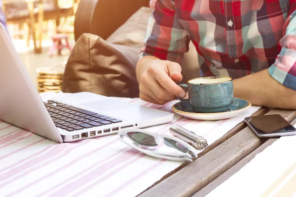 Cropped image of modern man with laptop and e-cigarette. Modern man sitting in cafe and drinking coffee.