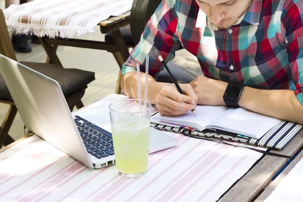 Closeup of man\'s hands  writting something in notebook diary. Phone, notebook diary, laptop and limonade are on table. Office desk idea concept.