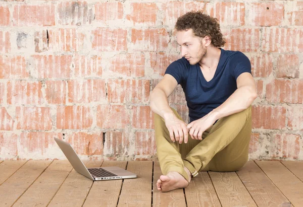 Hipster with a laptop in front of a brick wall. Handsome man working in room. Modern lifestyle