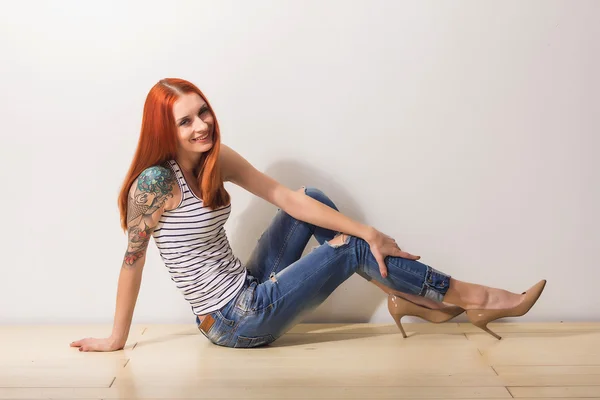 Laughing beautiful redhead woman with tattoo sitting on the floor and posing