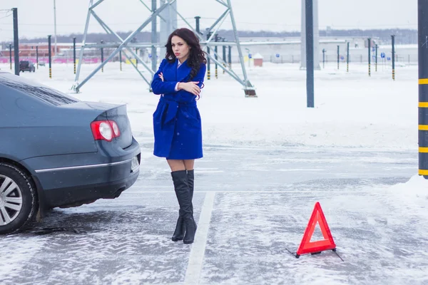 Attractive woman standing near her broken car next to a warning sign