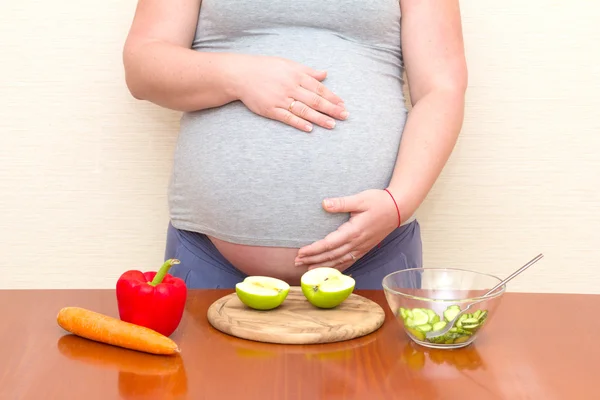 Pregnant woman and healthy food. Vegetables and fruit on the table against the background of the pregnant woman. Prenatal diet.