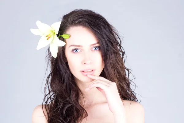 Woman with curly hair and big blue eyes touching lips. Woman with a flower in her hair.