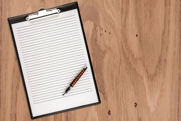 Clipboard with blank paper and pen on wooden desk. Copy space fo