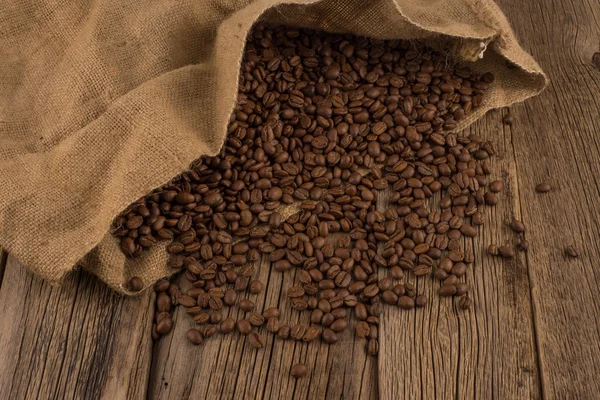 Coffee beans in coffee bag made from burlap on wooden surface