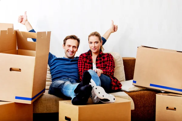 Happy tired couple sitting on couch in new home with cordboard boxes around