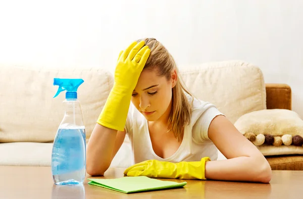 Tired young woman cleaning table in yellow gloves