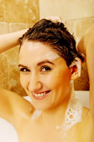 Young happy woman washing hair in bath