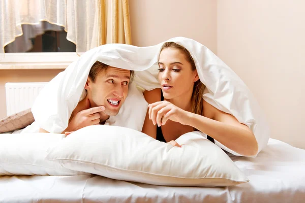 Young couple lying on bed under quilt