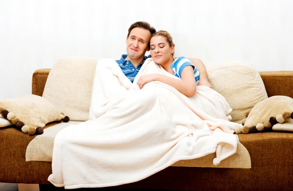 Smiling loving couple sitting on couch with blanket