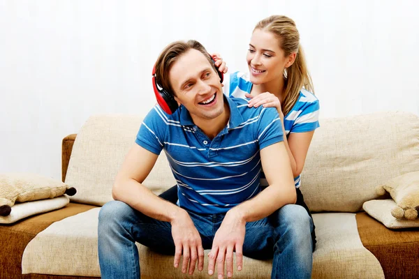 Couple relaxing on the sofa, man listening music woman hugging him