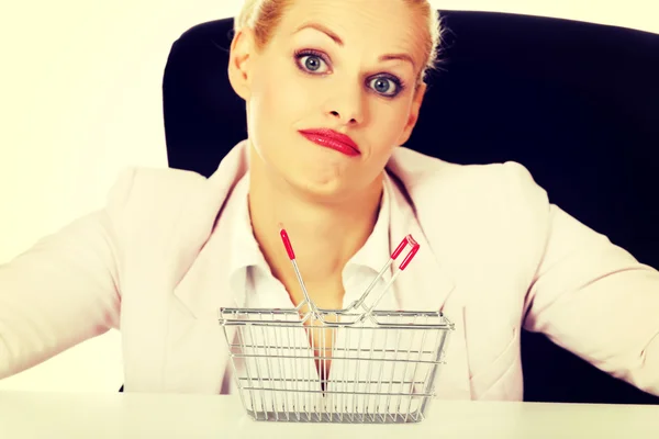 Surprised business woman sitting behind the desk with small shopping basket