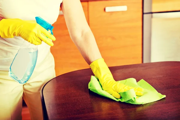 Elderly woman in yellow gloves cleaning table