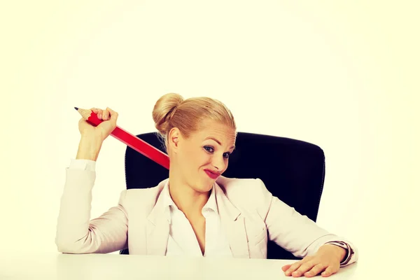 Young business woman sitting behind the desk and holding big pen