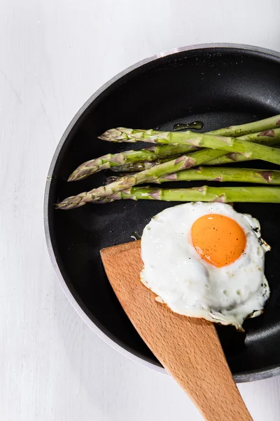 Green asparagus with fried egg on the frying pan
