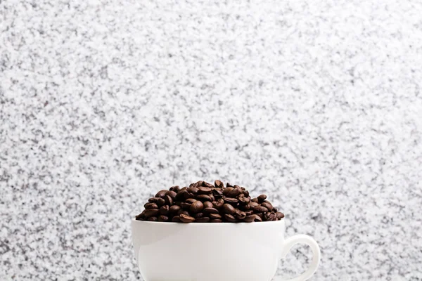 White cup with coffee seeds on granite background