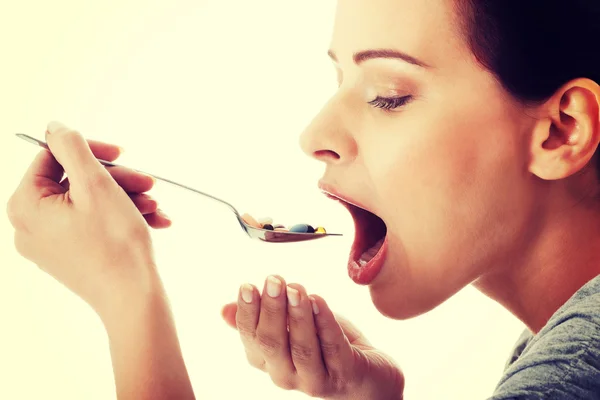 Young casual woman eating pills on a spoon.