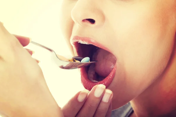 Woman eating pills on a spoon.