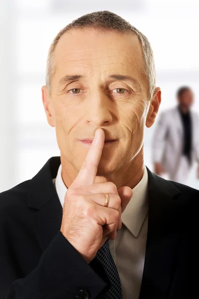 Mature man with finger on lips.