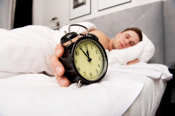 Man with alarm clock in bedroom.