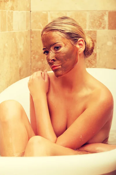 Woman sitting in bath with chocolate face mask