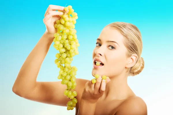 Side view of nude woman eating grapes, looking at the camera