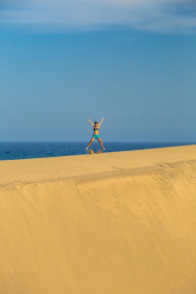 Woman with arms up outstretched jumping on sand desert dunes