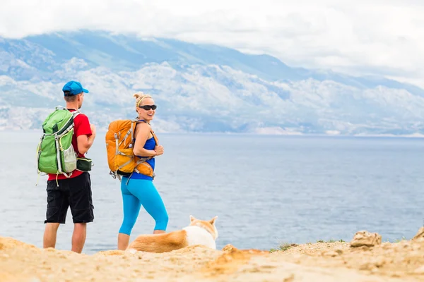 Couple hikers walking with dog at seaside and mountains