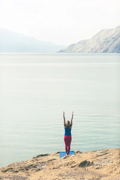 Woman meditating in yoga tree pose at the sea and mountains