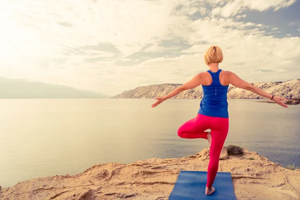 Woman meditating in yoga tree pose at the sea and mountains