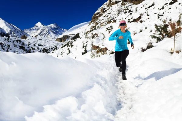 Woman trail running on snow in winter mountains