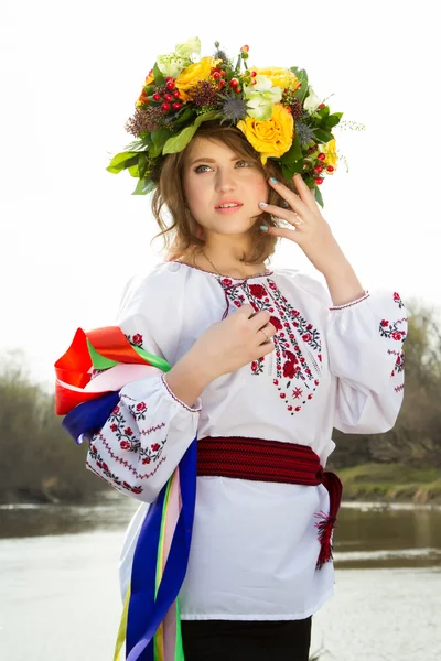 Girl in an embroidered shirt and a wreath on his head standing on the river bank