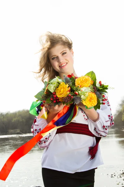 Girl in an embroidered shirt and a wreath of fresh flowers on the river bank
