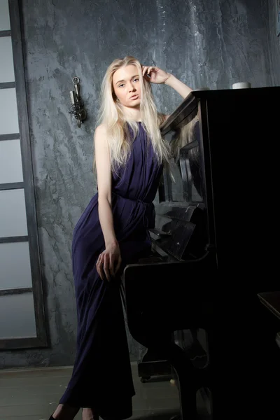 Young blond woman in evening dress standing at the piano