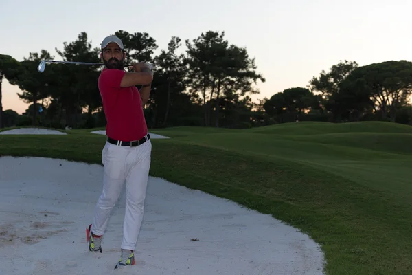 Golfer hitting a sand bunker shot on sunset