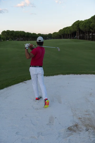 Golfer hitting a sand bunker shot on sunset