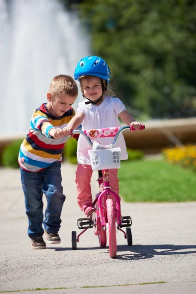 Boy and girl in park learning to ride a bike