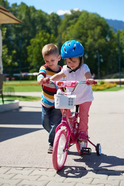 Boy and girl in park learning to ride a bike