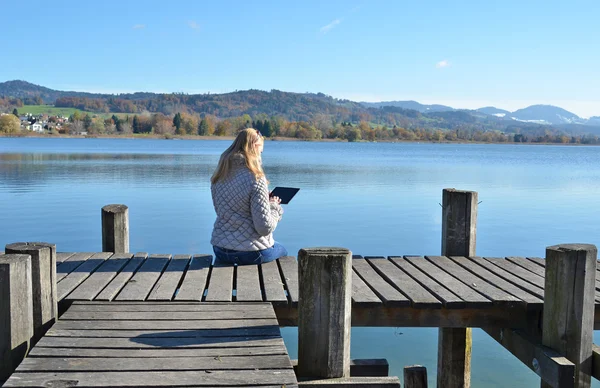 Girl reading  tablet  against  lake.