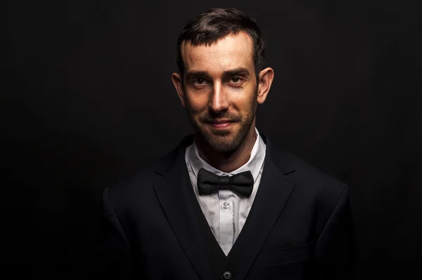 Fashionable man in siute and bow tie over dark background.
