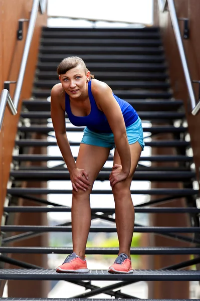 Fit woman resting after run on stairs smiling.