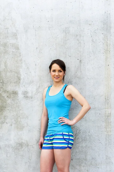 Girl in blue tank top and shorts over the wall smiling.