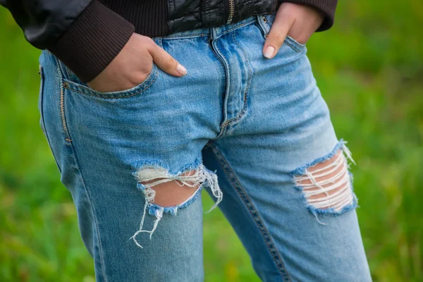 The girl holds hands in pockets torn jeans