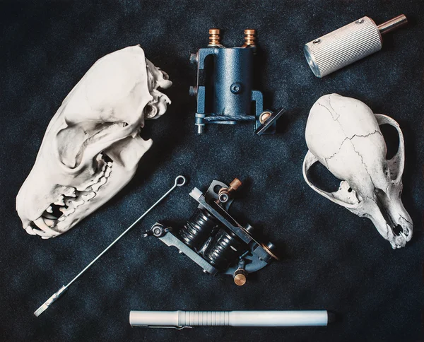 Two machines for tattoos with a needle and parts, gray marker drawing lie on black paralon shot closeup. On the sides are two skulls of animals foxes and dogs.