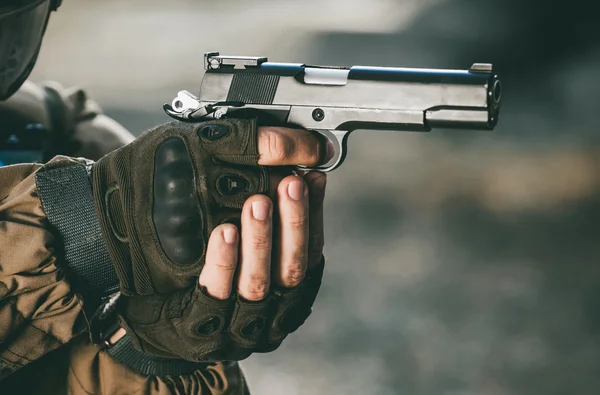 The soldier in the performance of tasks in camouflage and protective gloves holding a pistol with the hammer cocked takes aim for shot. War Zone.