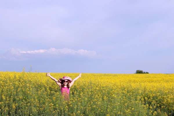 Happy little girl with hands up on yellow flower field