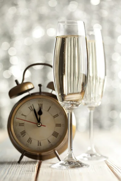 Glasses of champagne and alarm clock on wooden background