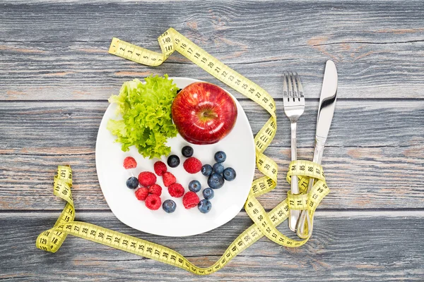 Fitness salad and measuring tape on wooden table.